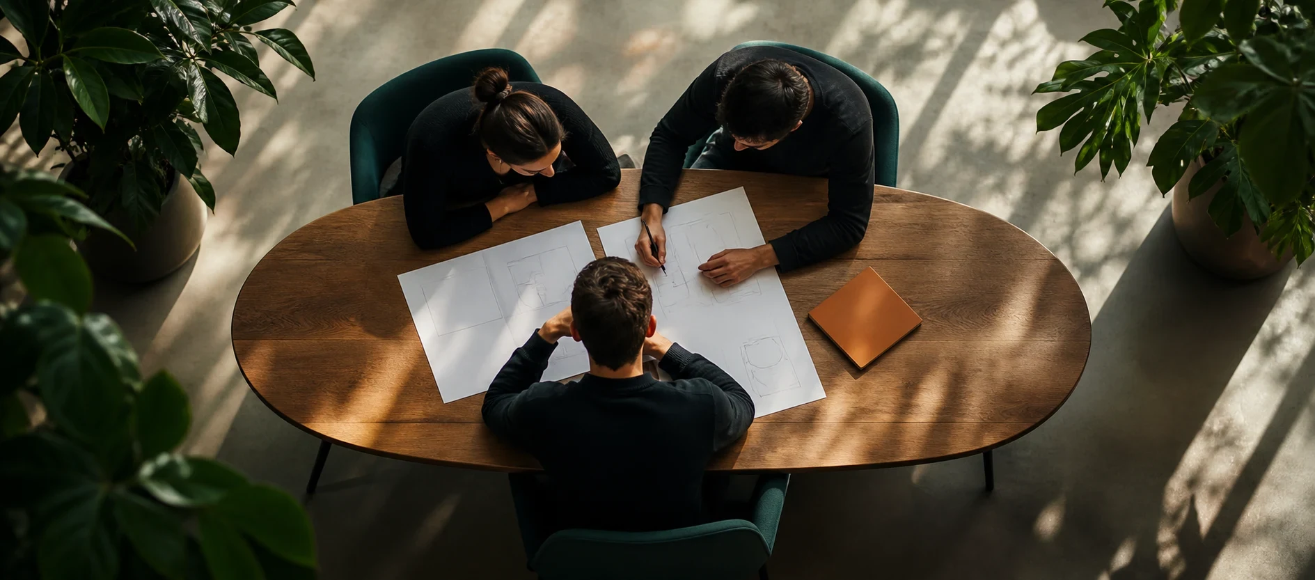 Three colleagues around an oval table working through printed diagrams, seen from above.
